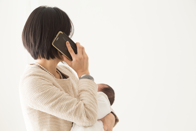 赤ちゃんを抱っこしながら電話する母親
